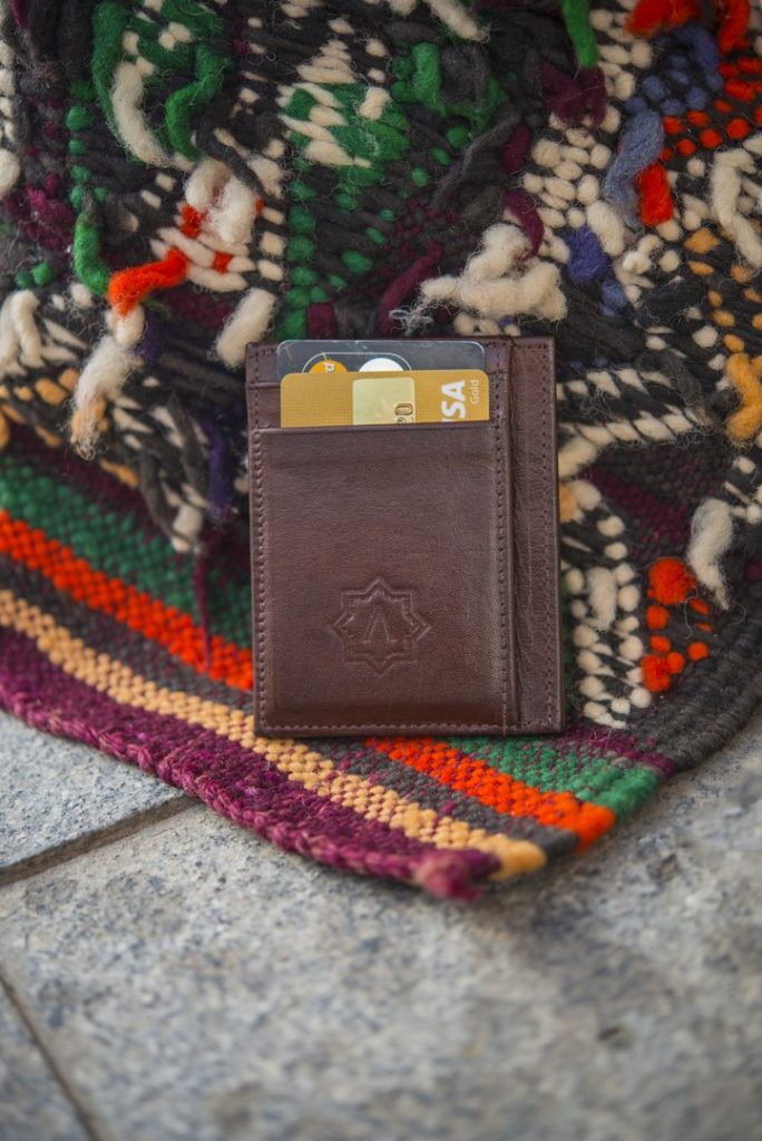 Brown leather wallet with bank cards resting on a colorful handwoven Moroccan rug, ADNA Wallet product shot
