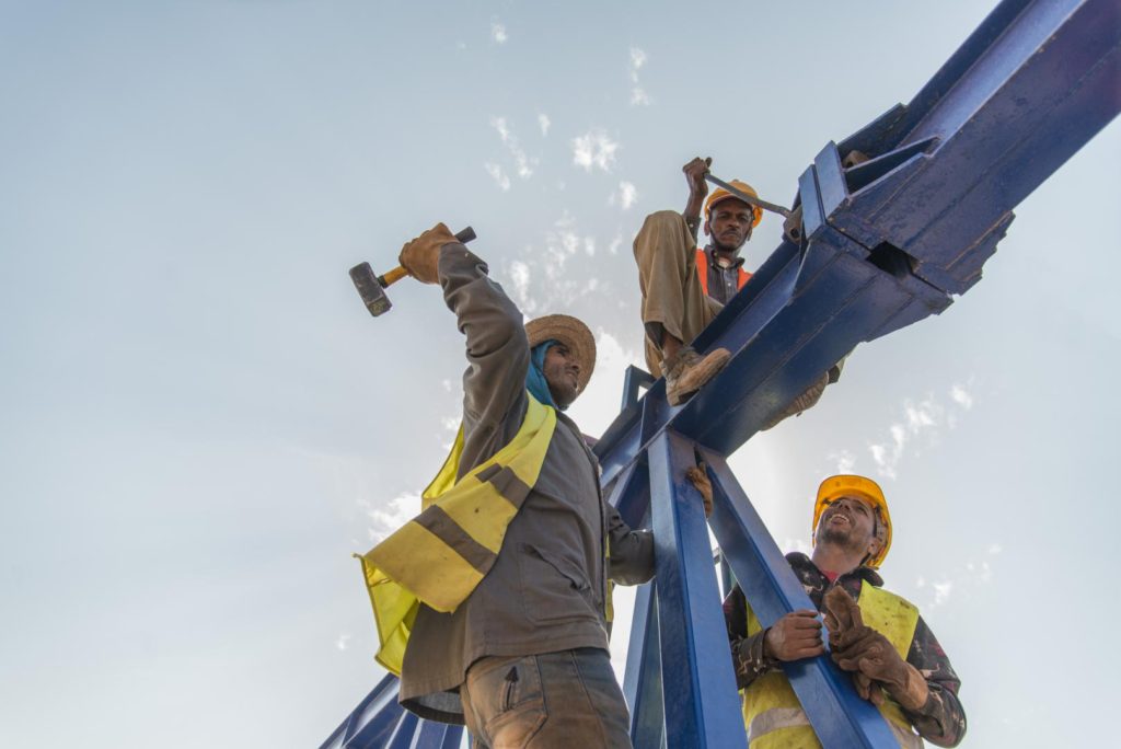 Construction workers in safety gear assembling steel beams on scaffolding, African Development Bank project