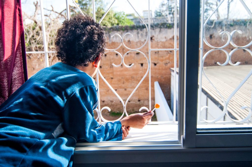 Child looking out through an ornate window grille, documentary photo for the Centre Lalla Meriem child protection association in Rabat