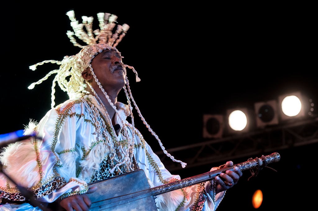 Performer in an elaborate white tasseled headdress singing on stage at the Gnaoua World Music Festival