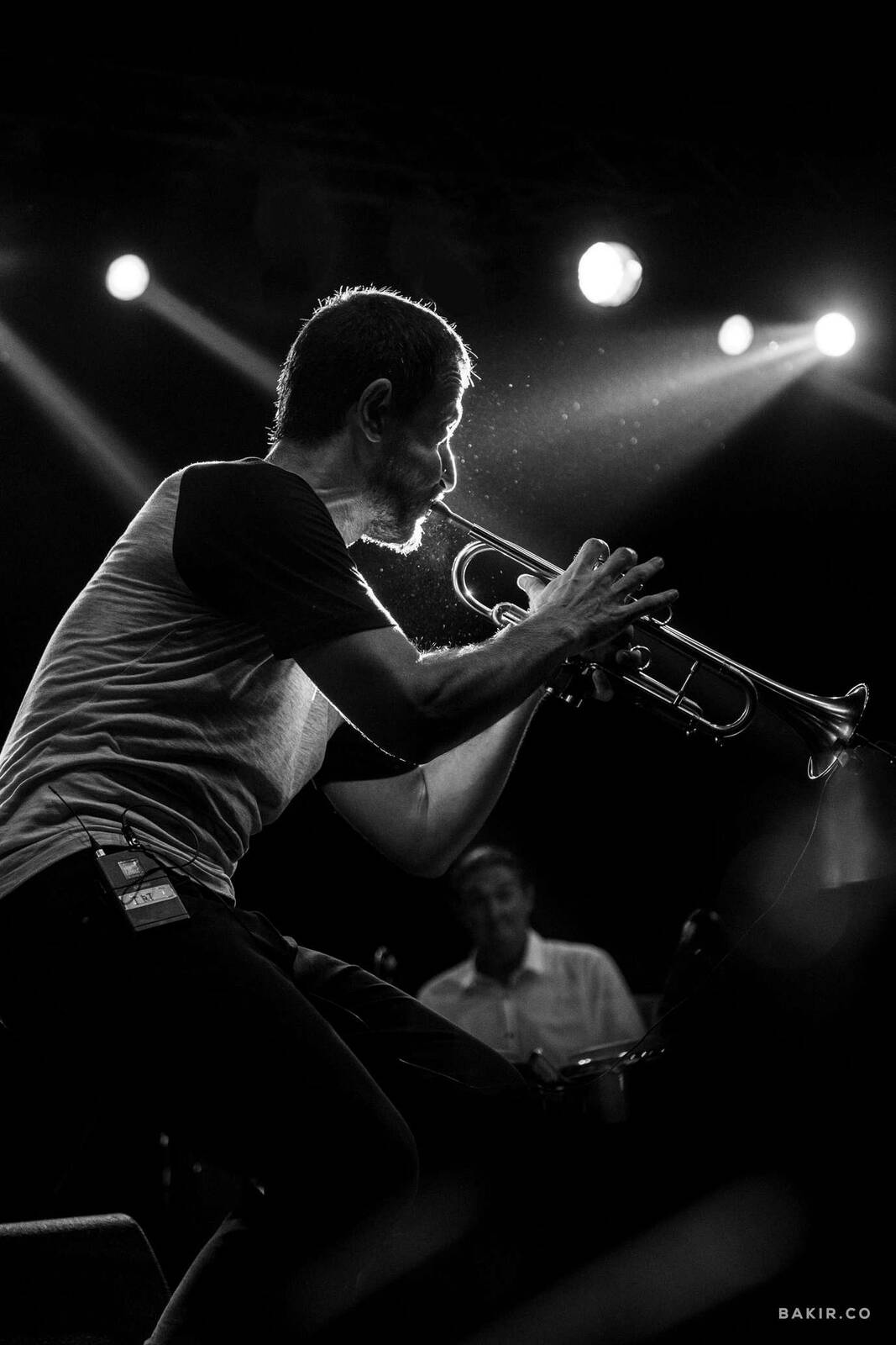 Black and white photo of a musician playing trumpet on stage under dramatic lighting