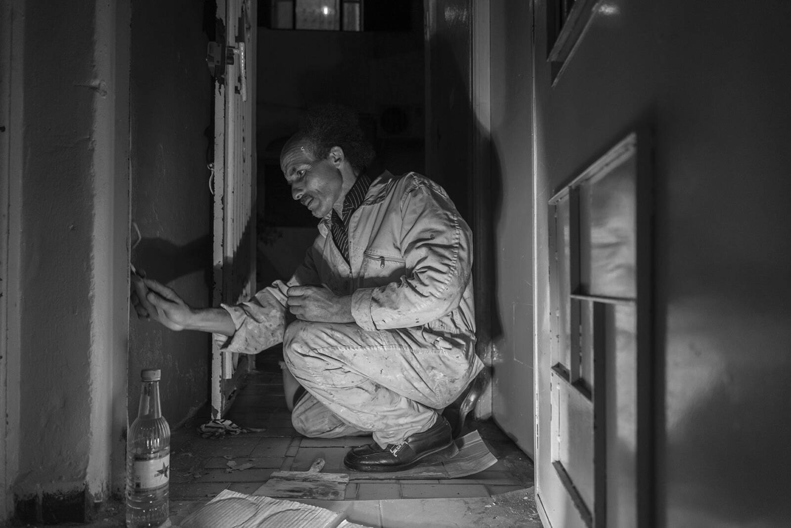 Black and white photo of an elderly man crouched, cleaning or working on the floor