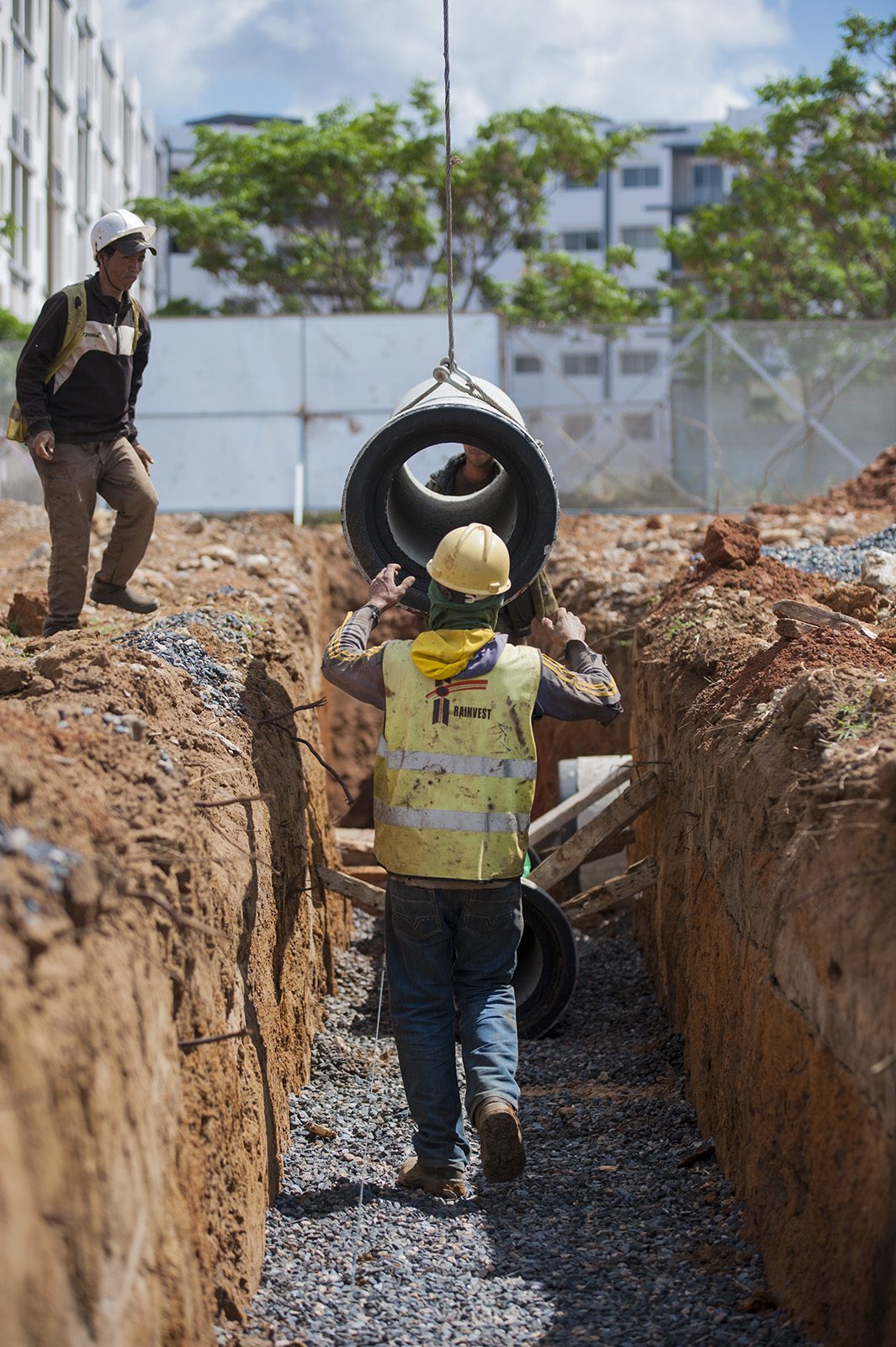 Construction workers on a job site lowering a pipe into a trench with a crane