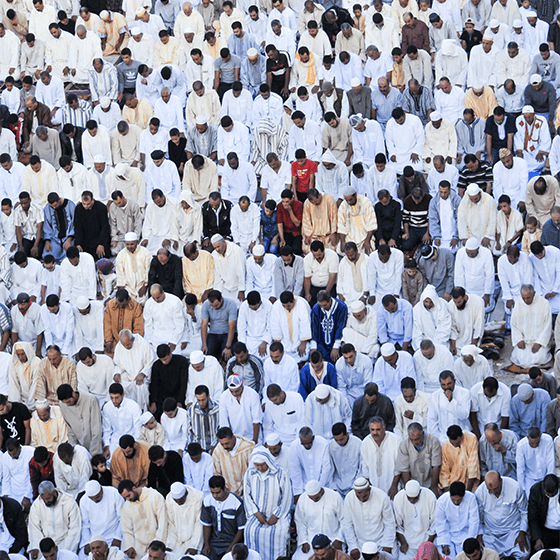 Large crowd of men in traditional white djellabas gathered outdoors for Eid al-Adha prayer