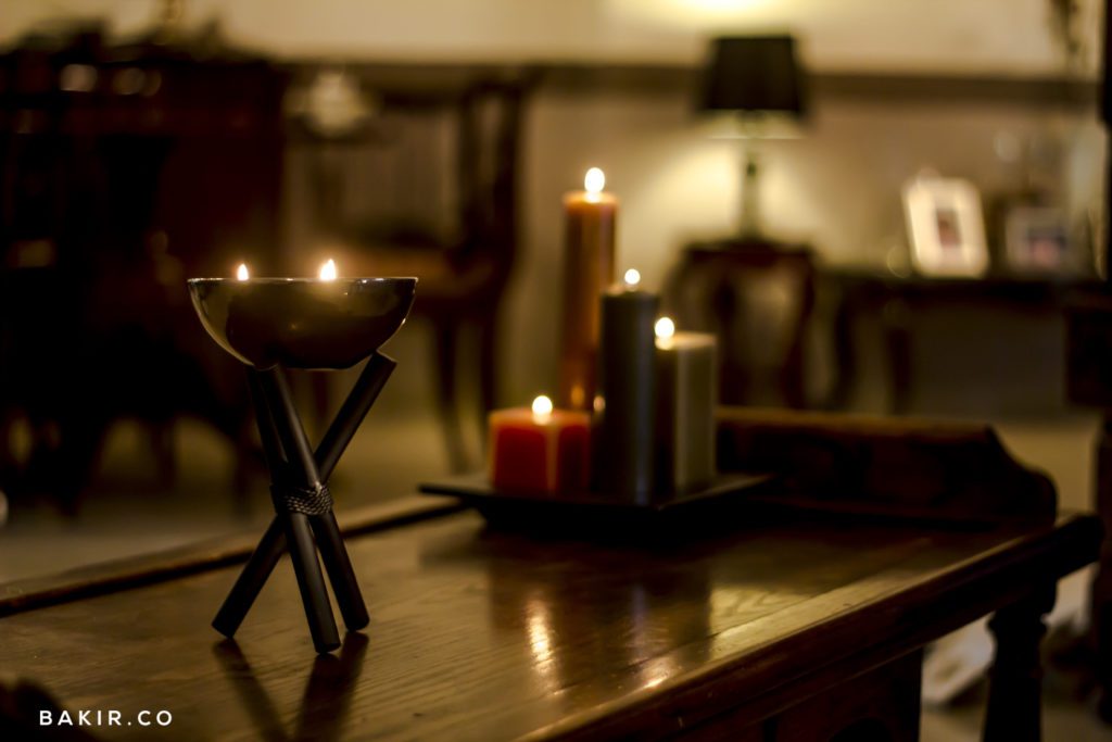 Lit scented candles arranged on a wooden stand in a warmly lit living room, Vellaluz lifestyle product shot