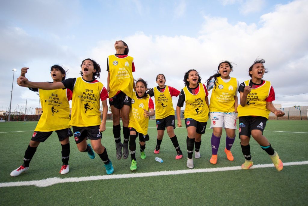 Girls' football team celebrating together on the field in yellow jerseys, Lead Morocco leadership program