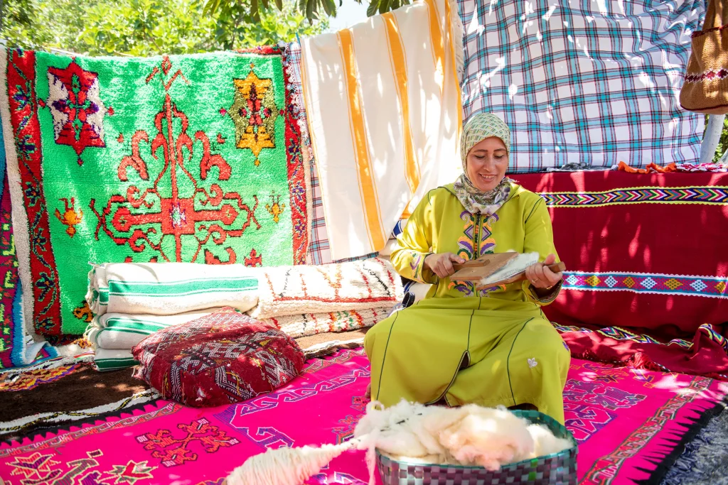 Woman in traditional yellow dress seated among handwoven Moroccan carpets, for a BMZ development program feature