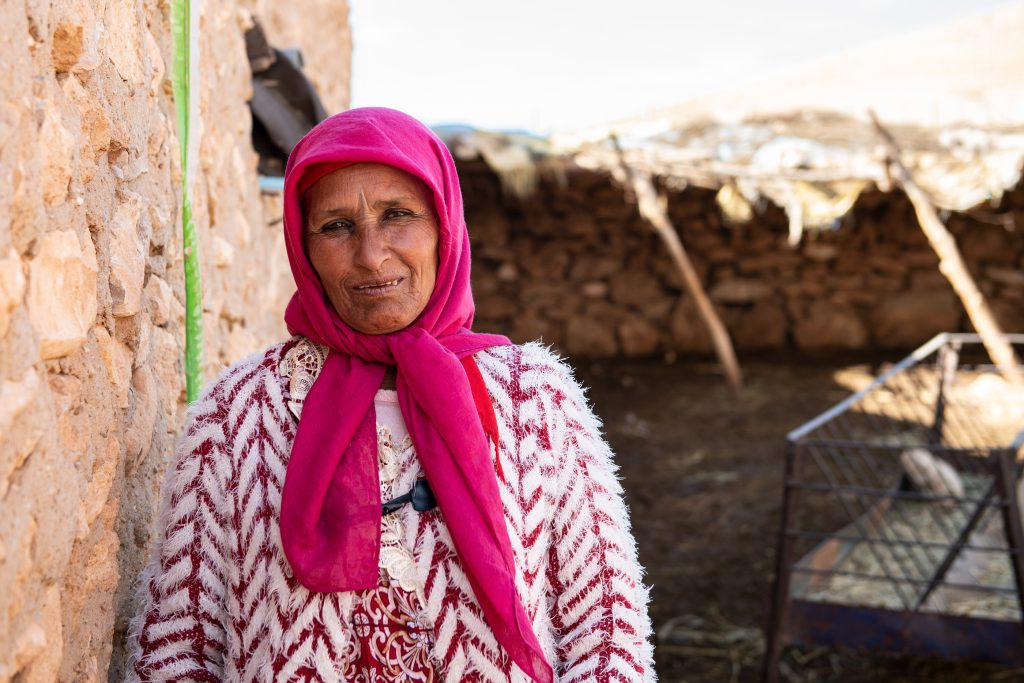 Portrait of a woman in a pink headscarf against a stone wall, part of an OXFAM Maroc portrait series